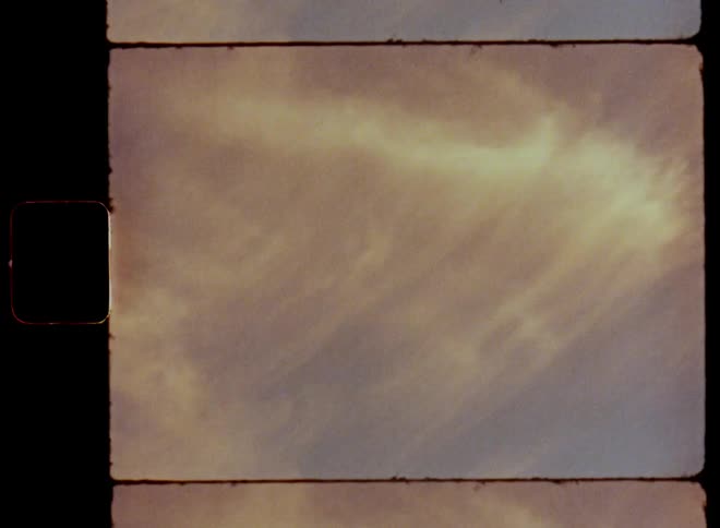Retro film footage with vintage vibes of the sun setting in the sky shining onto the hazy clouds colouring them red and orange in front of blue evening sky