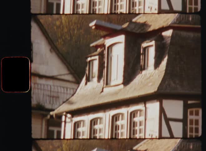 A view moving up from the center to the roof of a german style wood trimed home with dormer windows and window planters close to another home taken on old film