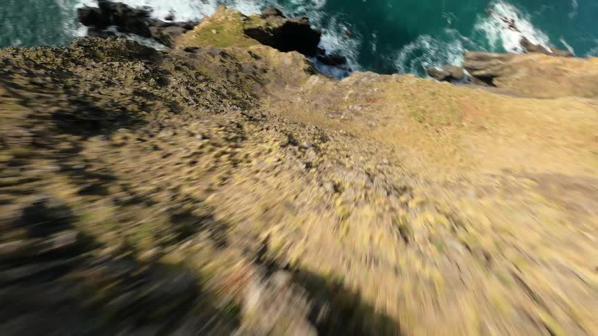 A dramatic highspeed FPV aerial shot where the camera dives quickly down an oceanside rocky cliff in the daytime