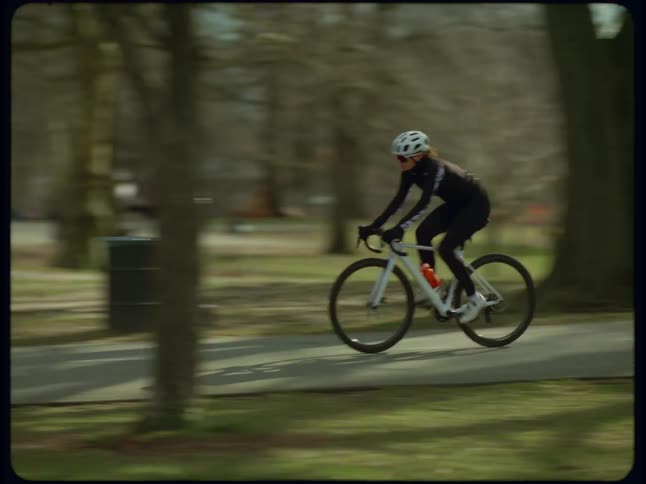 A woman wearing a cycling helmet is riding her bicycle through a park