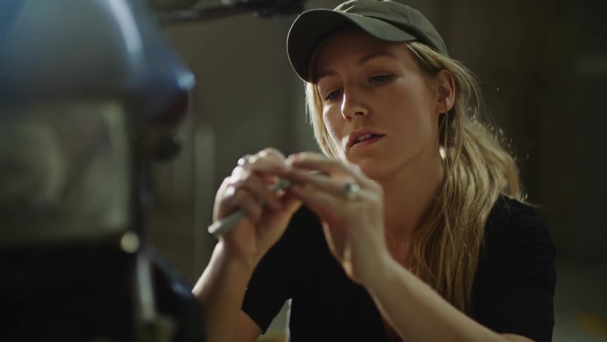 A woman wearing a black shirt sitting next to a motorcycle adjusting tools she is using