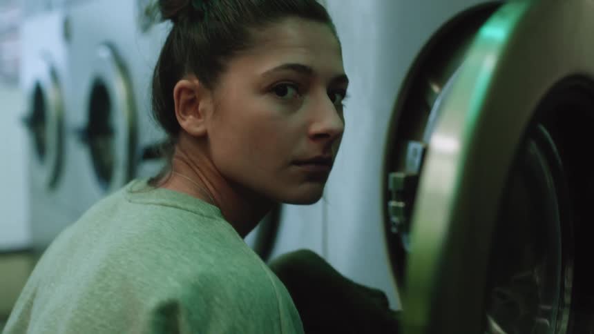 Woman looks around as she puts clothes in washing machine at laundromat