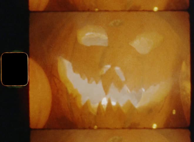 Rather static shot of smoke coming out of a scary carved Halloween pumpkin placed next to other Jack O'Lanterns and holiday decorations surrounded by brown oak leaves and branches and fairy lights