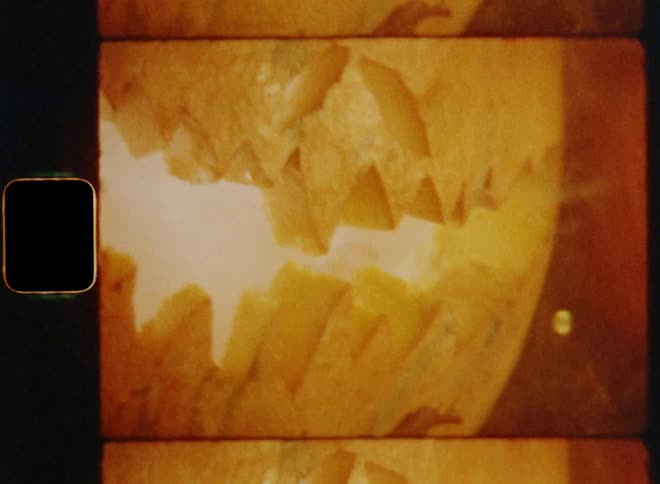 Old super 8mm film footage of the smoking mouth of a scary jack o lantern sitting in leaves placed on a decorative table with bright chain of lights with a slightly shaky dynamic handheld camera movement