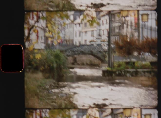 A stream flowing under a grey bridge with buildings in the background