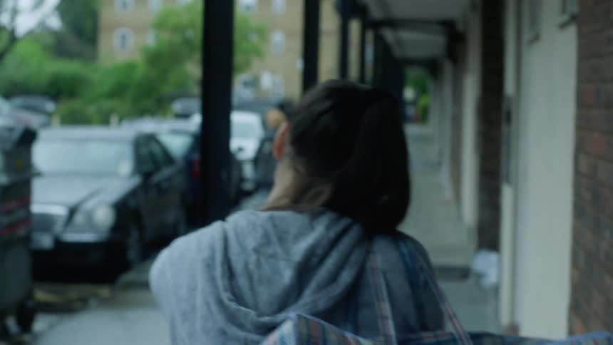 A young woman with a ponytail carrying laundry bag walking down a walkway to laundromat