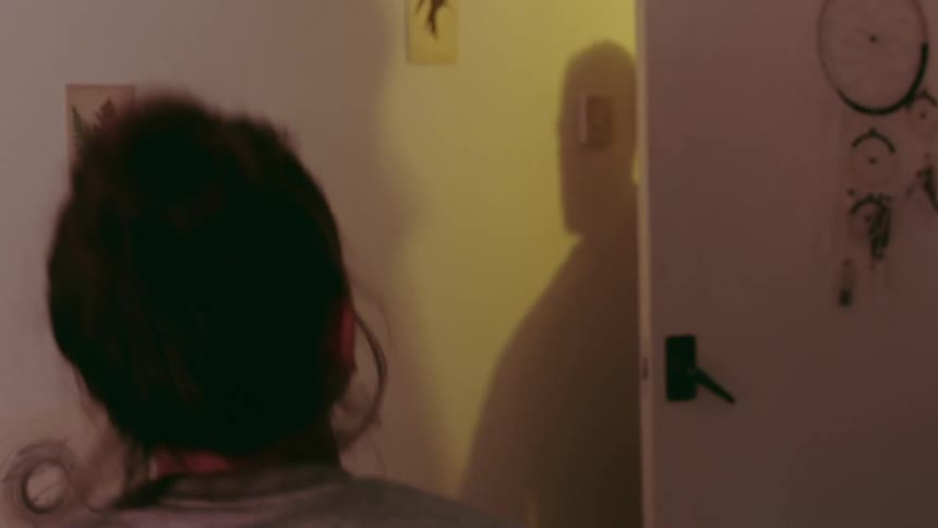 Woman with bra looks in mirror and rushes to put on gray sweater as the man with beard enters the room