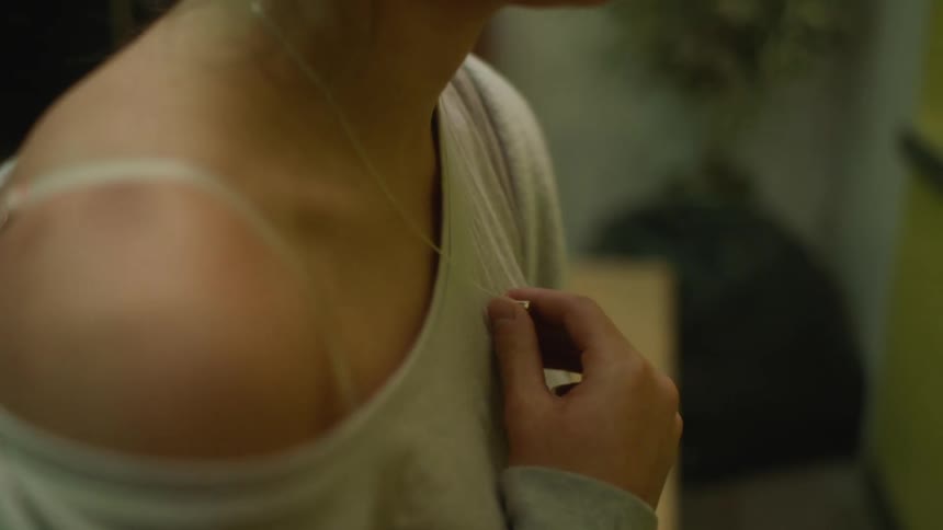 An up close of a womans shoulder while she plays with the necklace around her neck
