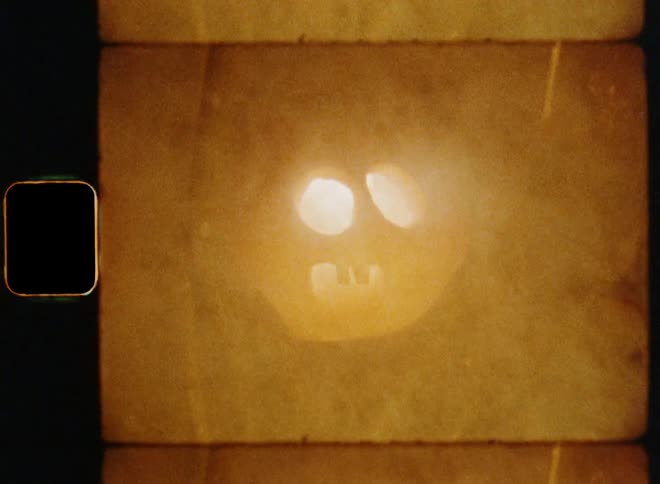 Retro 8mm film footage of orange pumpkin lantern with a burning candle outdoors surrounded by fog and tree branches causing an anxious feeling as a scary Halloween decoration