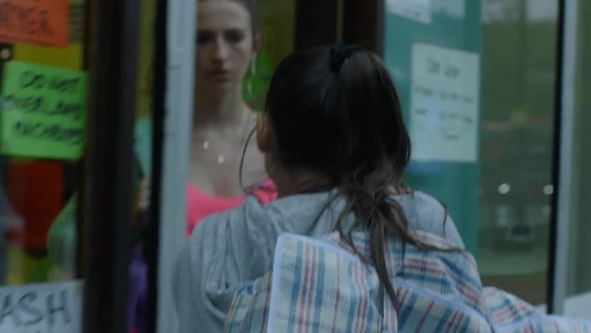 Woman carrying bag stares after woman she encounters at door to laundromat