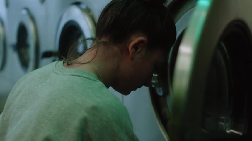 Woman with gray sweater loads washer with clothes in laundry shop