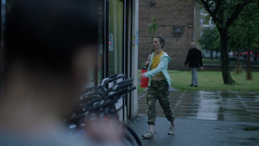 A woman is walking on a wet sidewalk carrying a shoulder bag as she walks into a building
