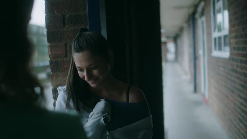 Woman smiles while she and another woman stand under covered walkway of upper floor of apartment building