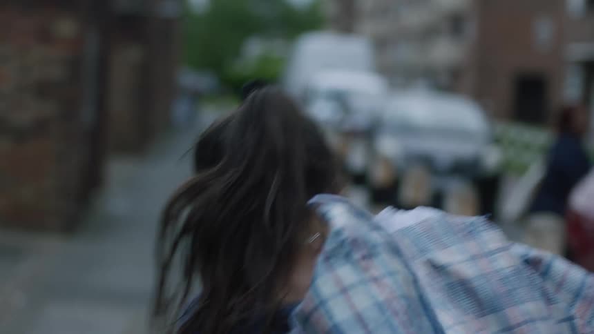 A teenage girl is rushing as she walks on a neighborhood sidewalk and struggling with the bag on her shoulder