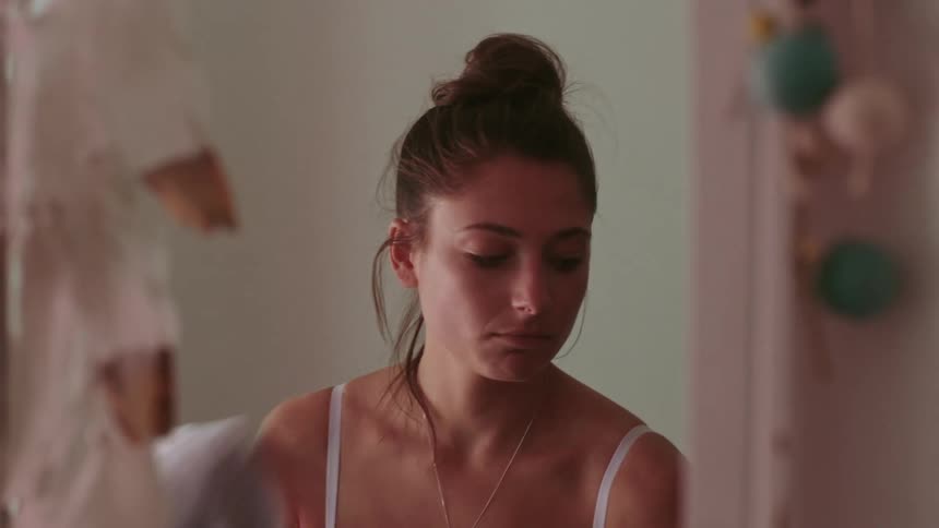Woman takes off gray sweater and looks at herself in the mirror