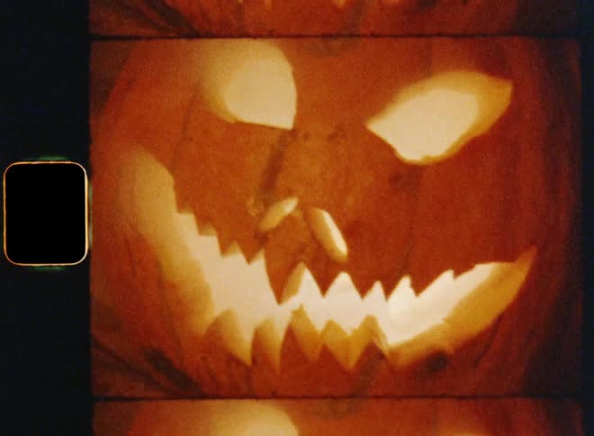 Dynamic handheld 8mm film of a terrifying carved angry Jack O'Lantern that is smiling and presenting his pointy teeth while standing on a concrete staircase in front of a house door on the thirty-first of October to celebrate all hallows eve