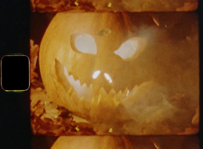 Smoke blown away by the wind or breeze fills the air as a carved pumpkin jack o lantern glows in the darkness with an evil and angry smile causing fear and a frightened feeling on vintage film