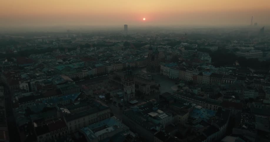 Aerial view of a crowded European town as automobiles move on the street and the sun sets on a foggy horizon