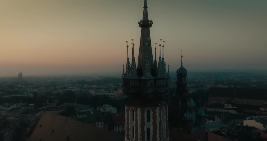 Cross on gothic church roof sits between two distinctly detailed towers in middle of foggy city scape