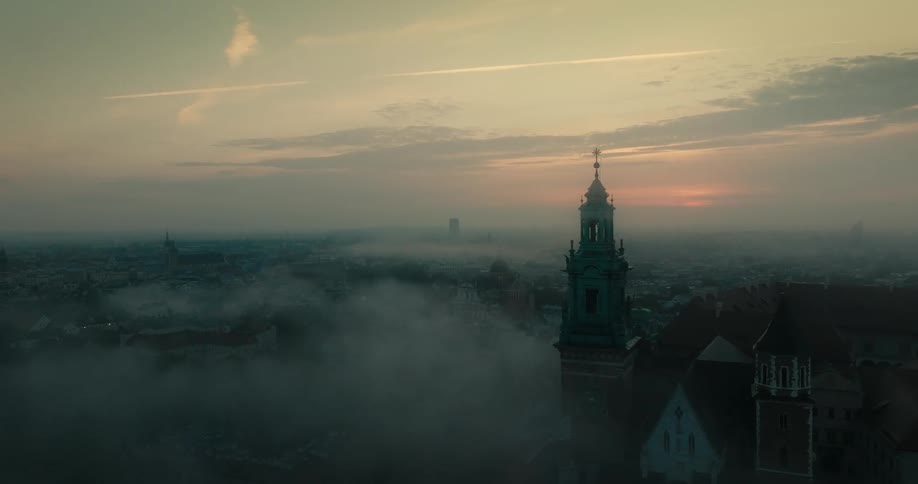 Aerial orbital view of the sunset sun behind the towers of a cathedral surrounded by mist
