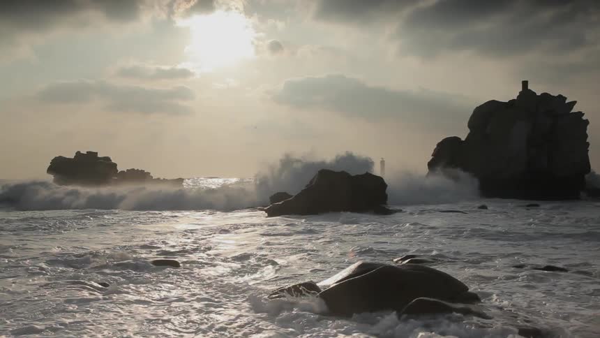 Waves crash over rocks and come toward shore at dusk