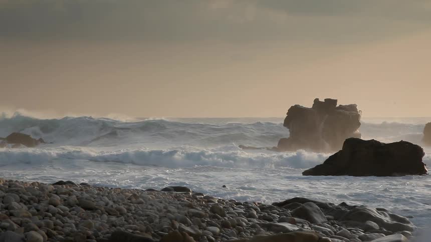 Waves crashing violently against rocks at dusk