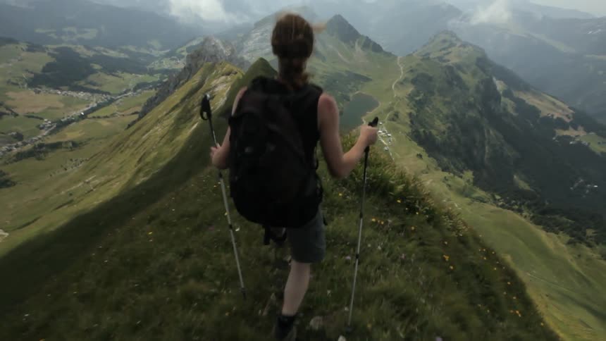 A female hiker is traversing a narrow ridge high up in the mountains