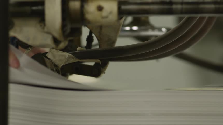 Machine arm moves paper along as worker guides paper