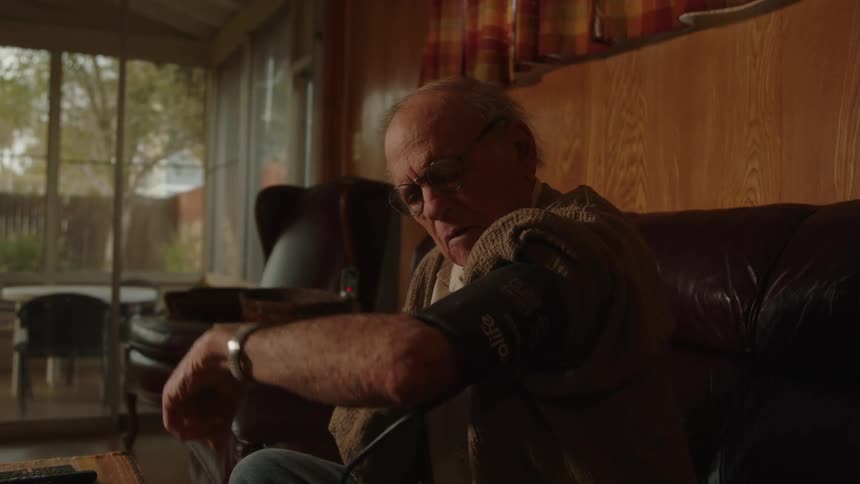 An old man puts on a blood pressure cuff and starts the machine