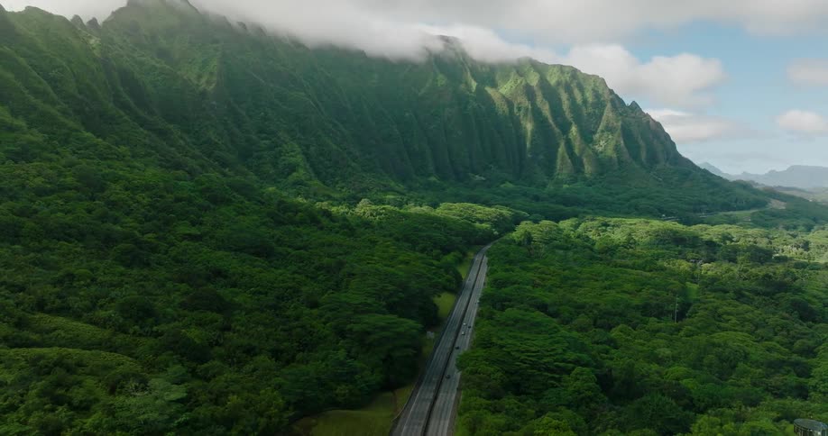 Aerial view of vehicle driving on highway through forest near the high mountain