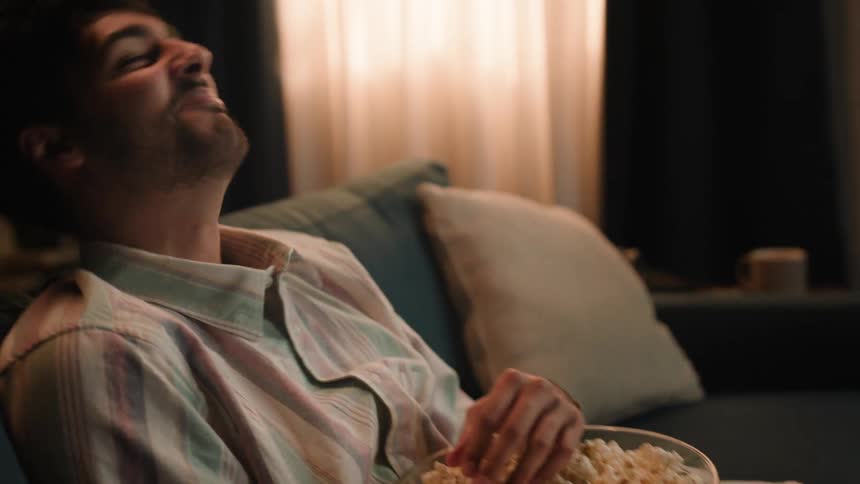 A young white man is sitting down and is eating some popcorn