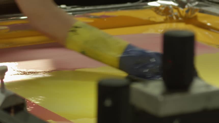 Worker wearing rubber gloves cleaning a printing screen on a factory