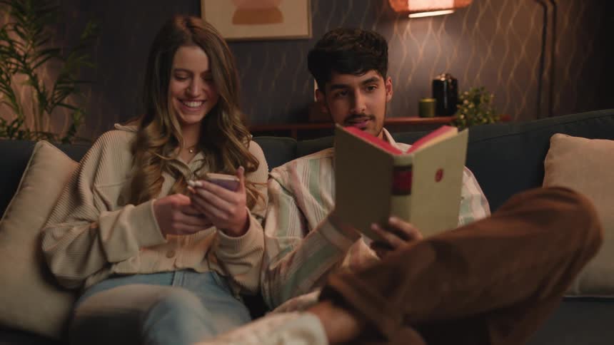 A young couple is sitting on the couch and reading a book