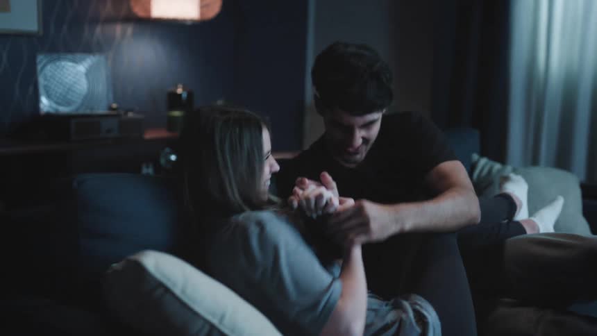 A woman taking a picture of a man sitting on the couch next to her as he turns and playfully tries to grab her phone