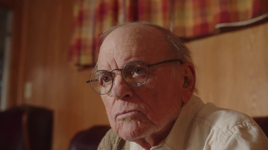 A close up of an older mans face wearing glasses as he looks off contemplatively