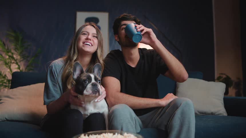 A man and woman pet their dog and watch something