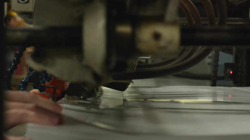 An up close of a factory machine as a persons hand feed the product