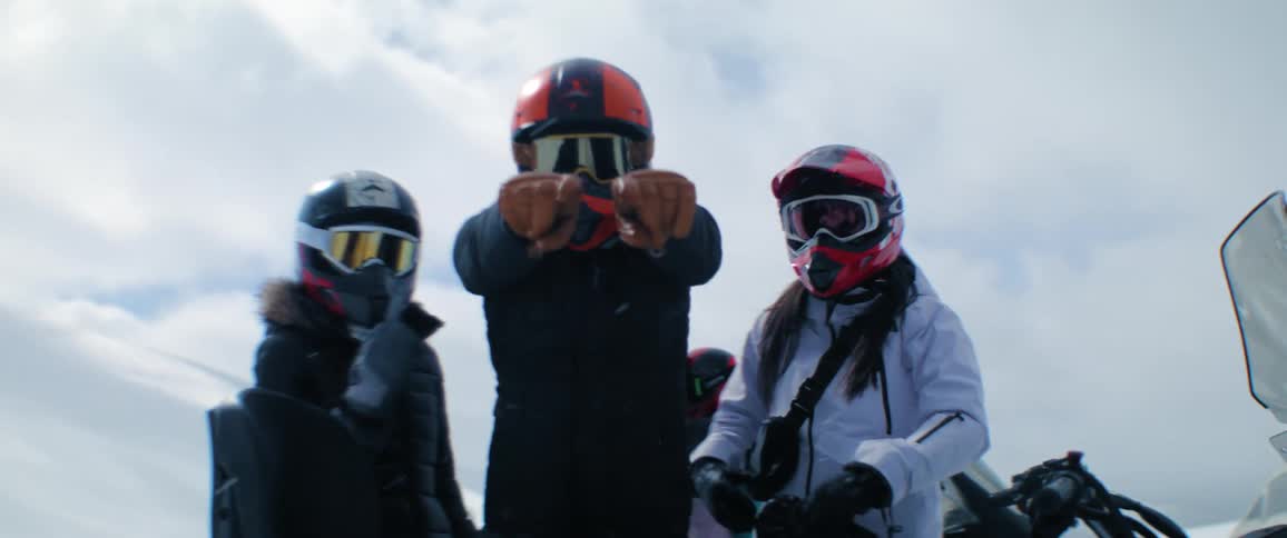 Friends wearing helmets and coats pose near snowmobiles as it snows