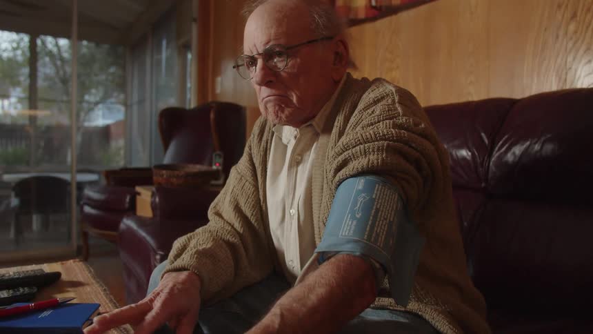 An older elderly man is sitting down indoors waiting impatiently for his blood pressure results