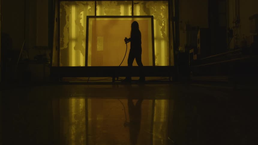Silhouette of a worker wearing a full body protective suit sprays a room with a power washing machine