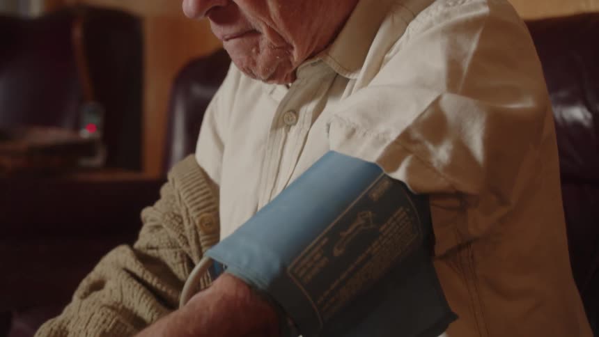 Elderly man sitting on a couch at home looking at a blood pressure monitor in the coffee table