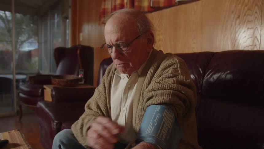 An older elderly man is sitting down and taking his blood pressure