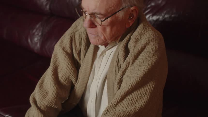 An old elderly man is sitting down inside of his home