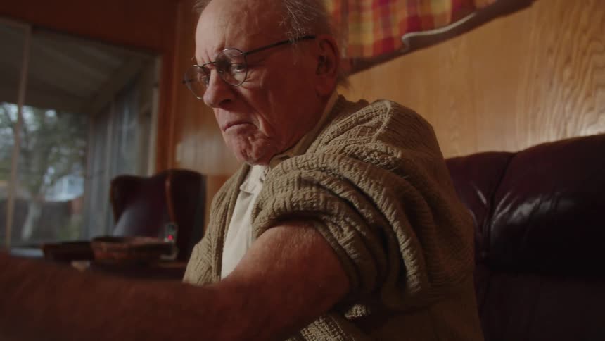 Elderly man sitting on a couch at home takes his blood pressure with a machine