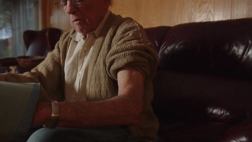 An older man wearing glasses sitting on his couch while putting a blood pressure cuff on his arm
