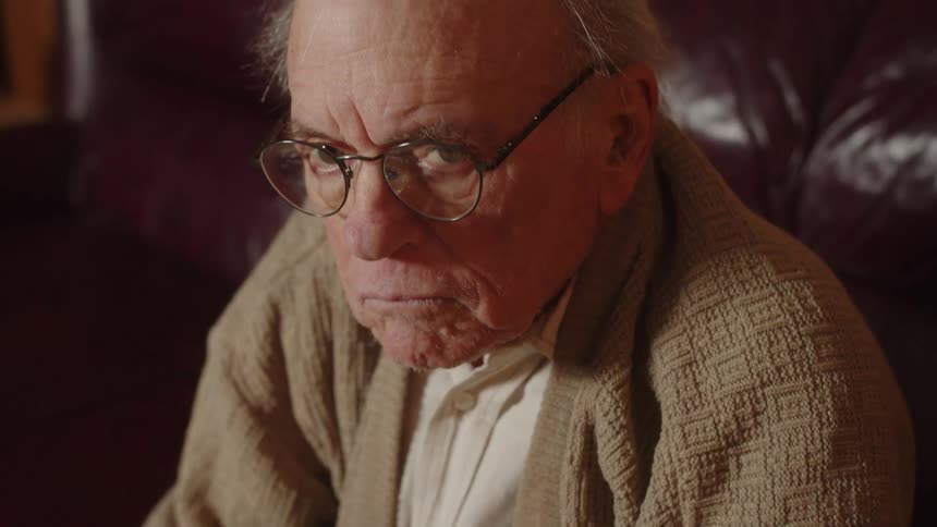 Elderly man sitting on a couch at home looking at the camera