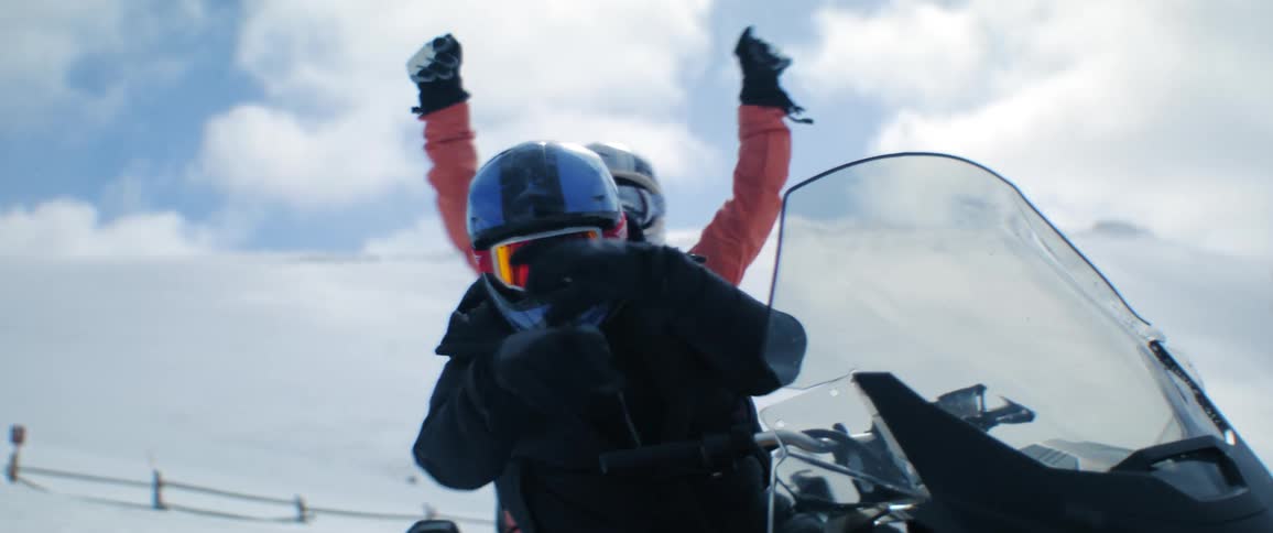 A male and female on a snowmobile raising their arms in celebration