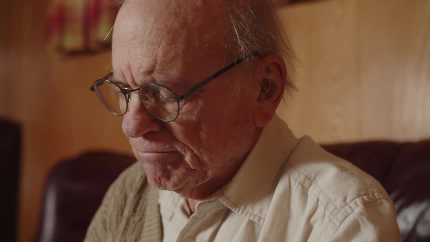 Elderly man sitting on a couch at home takes his blood pressure with a machine
