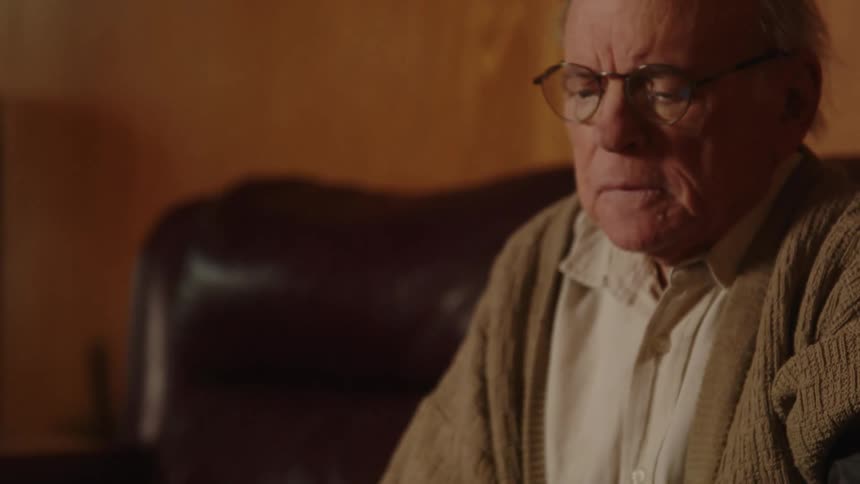 Elderly man sitting on a couch at home looking at a blood pressure monitor in the coffee table