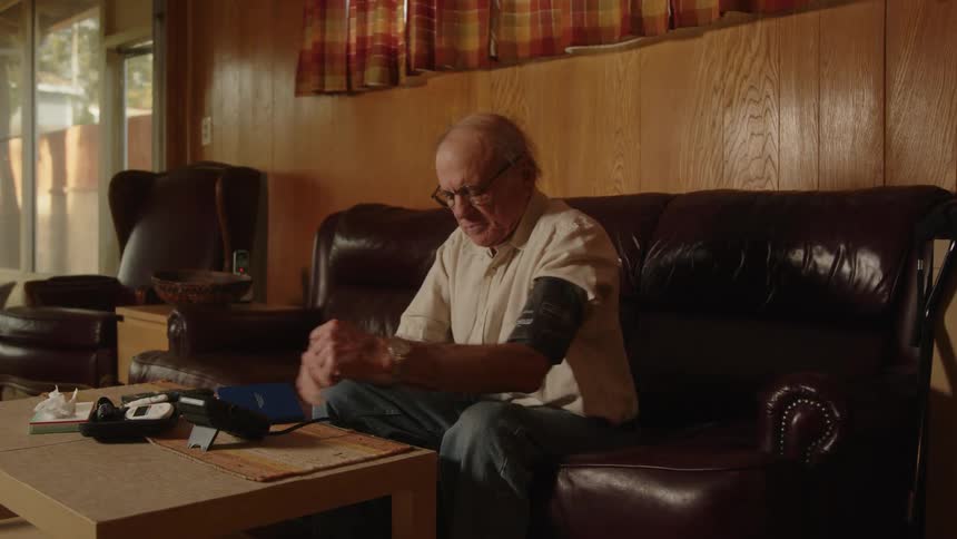 Elderly man sitting on a couch at home takes his blood pressure with a machine